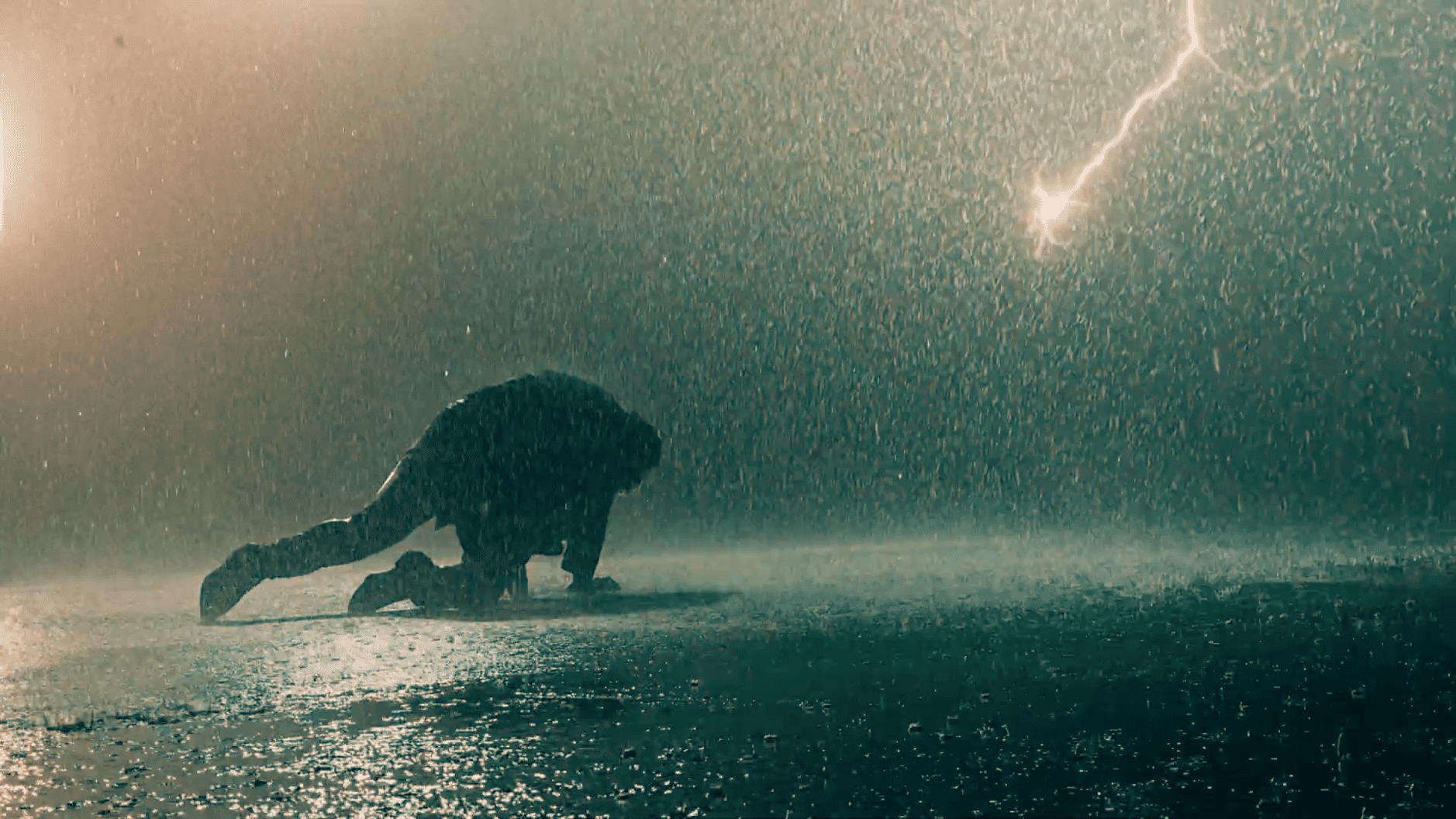 Das Bild zeigt eine Person, die bei starkem Regen auf dem Boden kniet. Im Hintergrund ist ein Blitz zu sehen, der die Szene dramatisch beleuchtet. Die Atmosphäre wirkt intensiv und emotional.