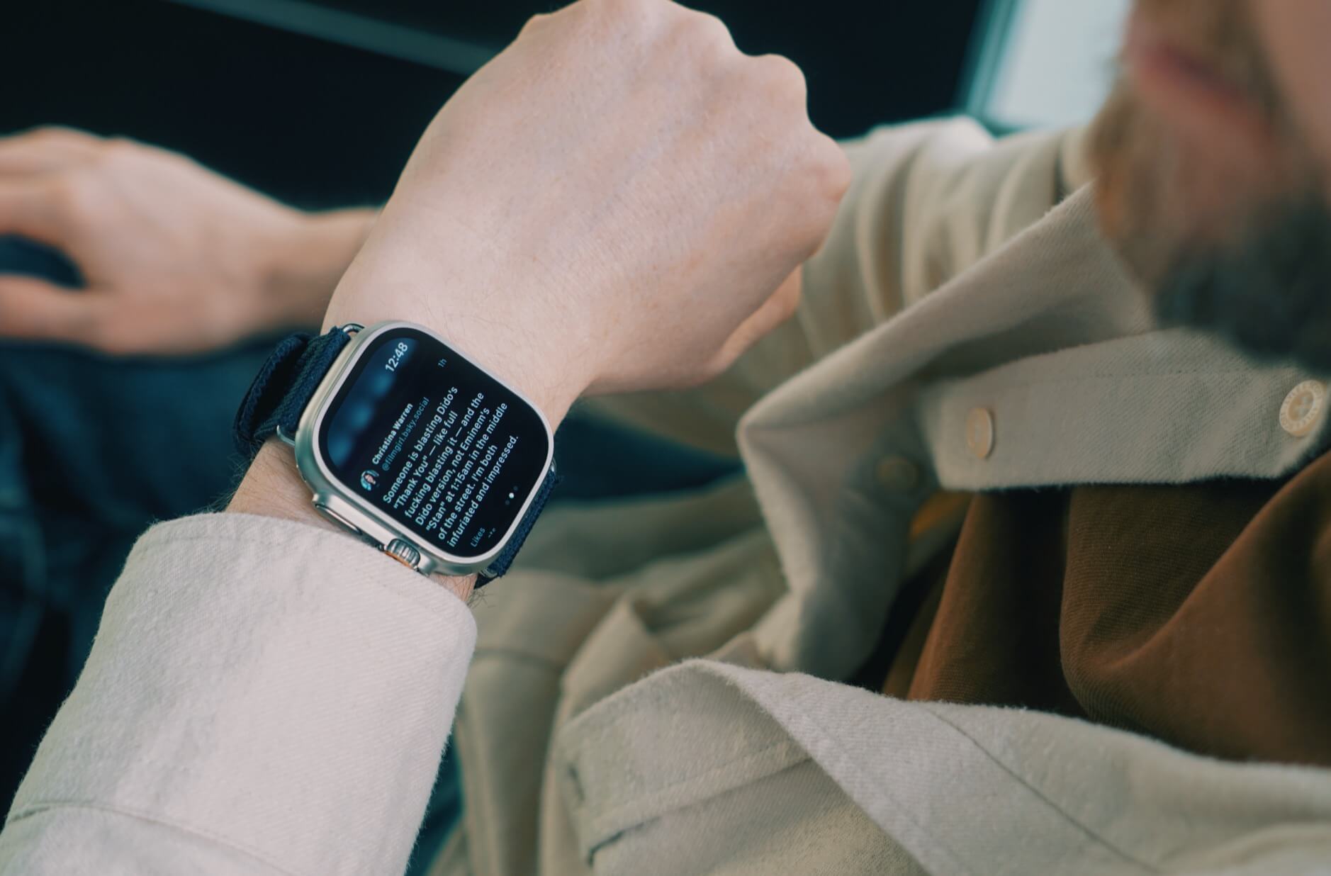 Smartwatch zeigt eine Nachricht auf dem Display, getragen am Handgelenk einer Person in beiger Kleidung. Text: "Someone is developing (…) of trust is important." Uhrzeit: 12:48.