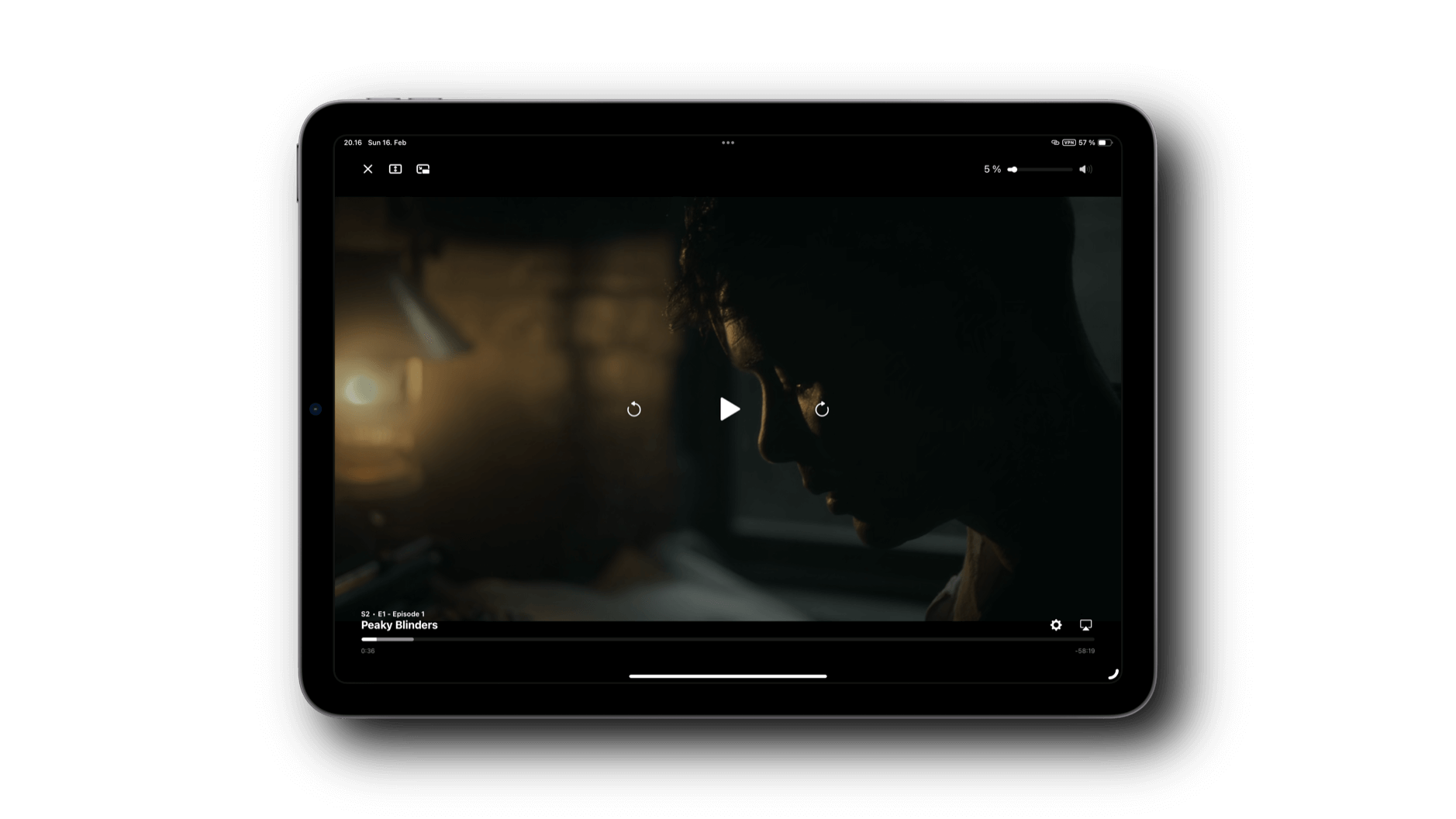 Das Bild zeigt ein Tablet, auf dem eine Szene aus der Serie Peaky Blinders abgespielt wird. Die Darstellung ist dunkel und zeigt eine Person im Profil, beleuchtet von einer schwachen Lichtquelle im Hintergrund. Unten auf dem Bildschirm ist der Titel „Peaky Blinders“ sowie die Episoden- und Staffelnummer (S2 - E1) zu sehen.