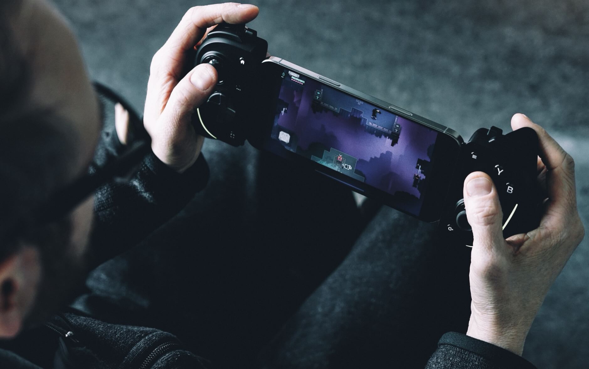 Auf dem Bild sieht man eine Person, die mit einem Gamecontroller ein Handyspiel spielt. Das Spiel auf dem Bildschirm erinnert an "Hyper Light Drifter". Die Person scheint in das Spiel vertieft zu sein.